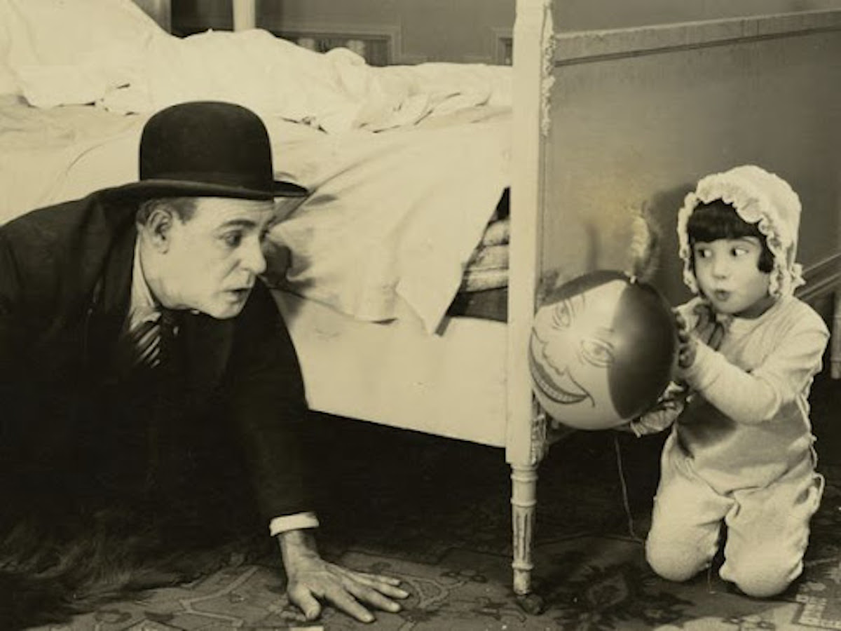 little girl in bonnet holding a ball behind bed with man crawling towards her