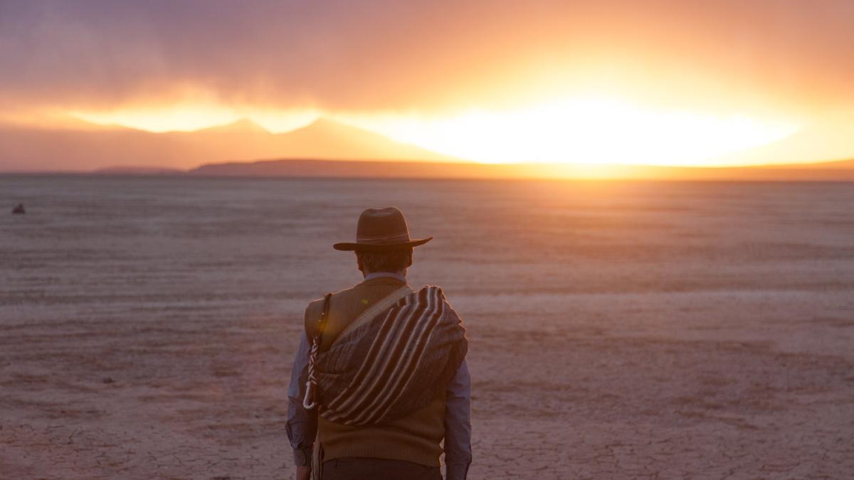 man with desert hat facing towards the sunset in the distance