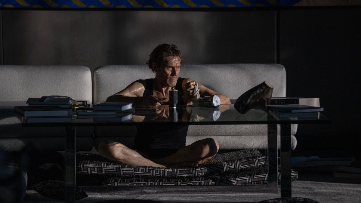 man wearing no shirt sitting on floor in front of coffee table eating