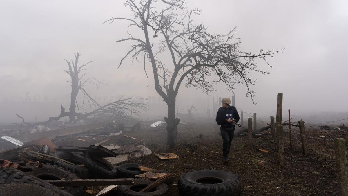 man holding camera walking through rubble and foggy field
