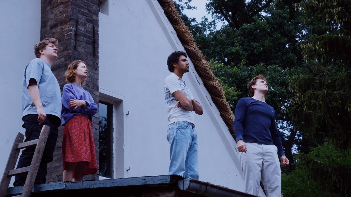 four young people standing on rooftop looking toward sky