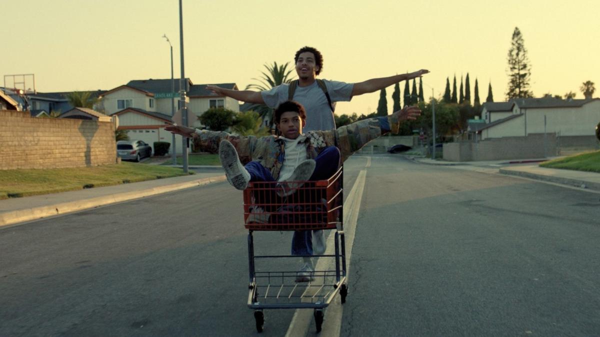 two young boys riding in shopping cart down street