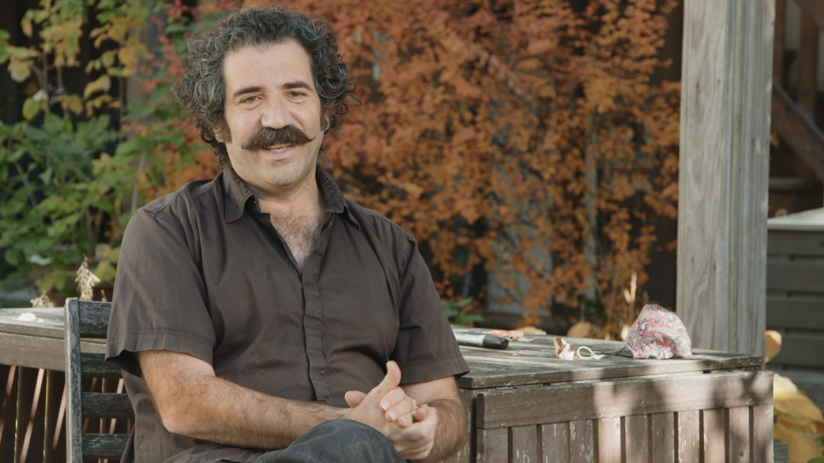 man with mustache sitting outside with fall leaves behind him