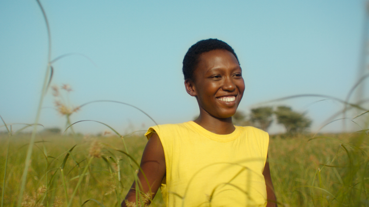 Black woman in yellow tank top smiling and walking through wheat field