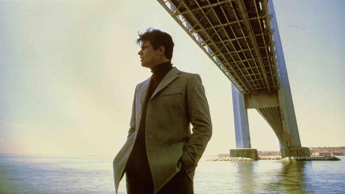 man in suit standing near water under bridge