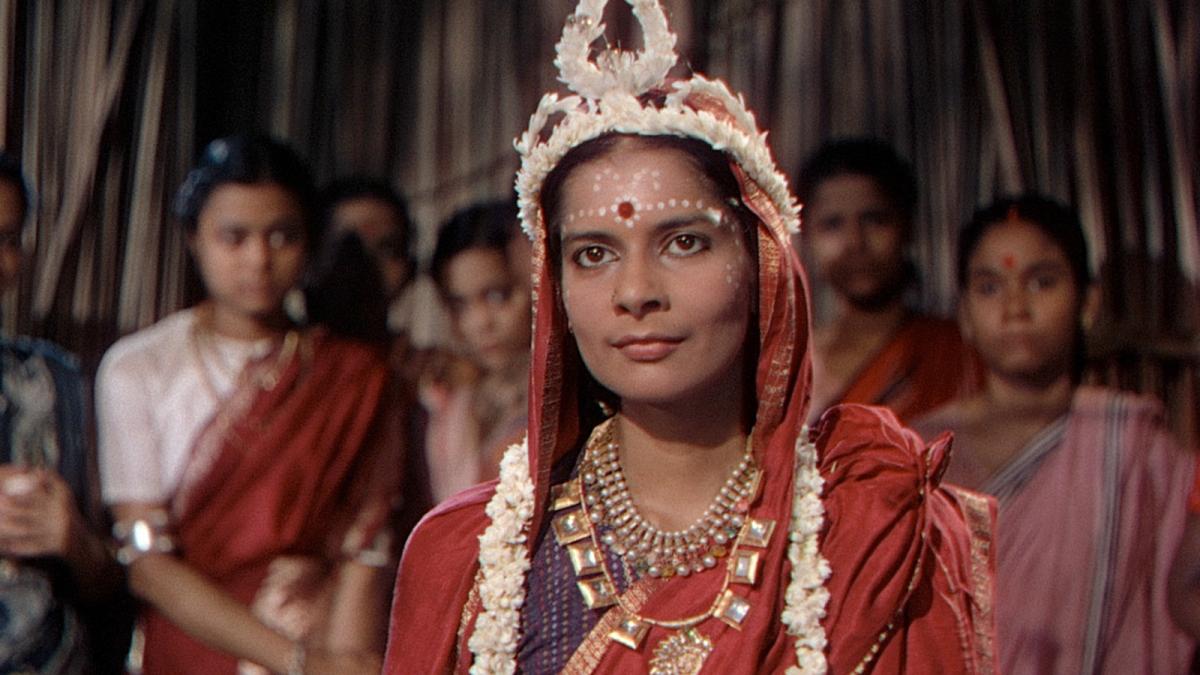 Indian woman in red garb and crown looking ahead with several women behind her