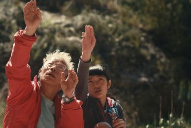 elderly man and young girl sitting outside with hands raised up and eyes to the sky