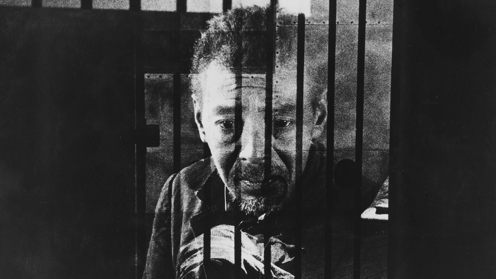 man looking out from bar covered window