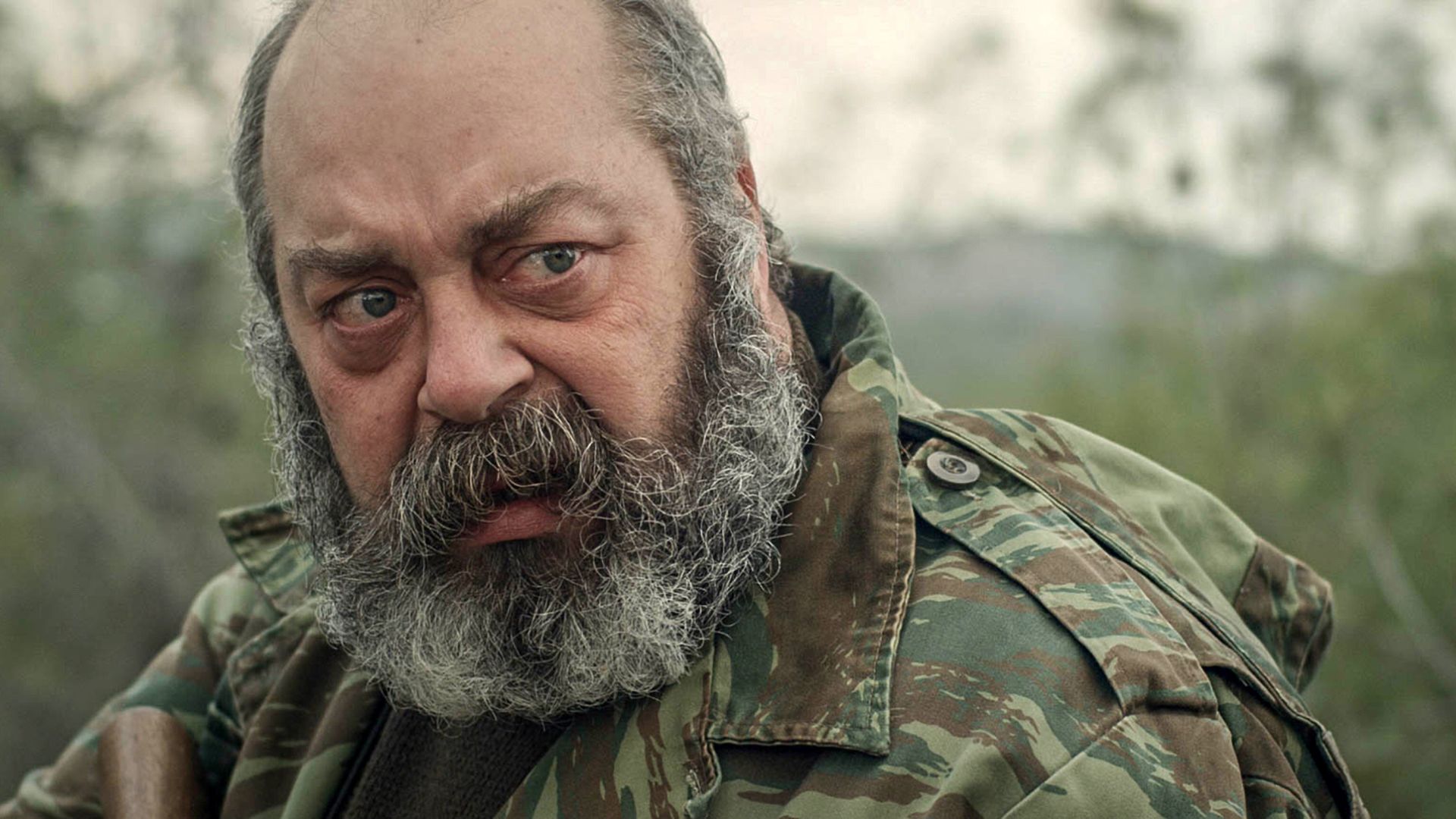 THE HUNT, man with dark and gray beard wearing camouflage jacket outside