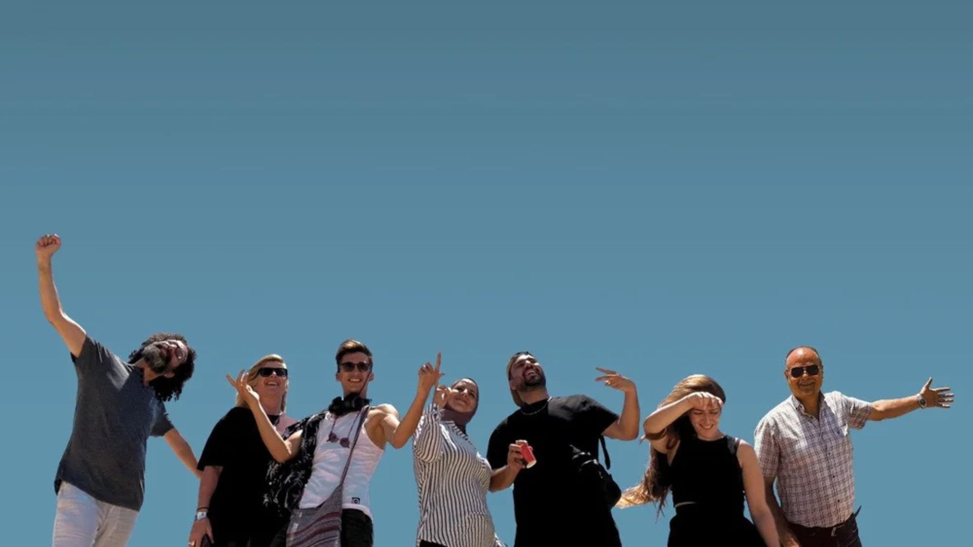 PALESTINE COMEDY CLUB, 2025, worm's eye shot of seven man standing with arms outstretched with blue sky behind