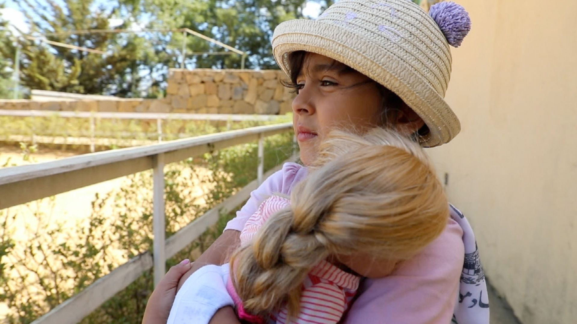 THE MIRACLE OF GAZA, 2025, young girl sitting on porch looking outside holding doll in arms
