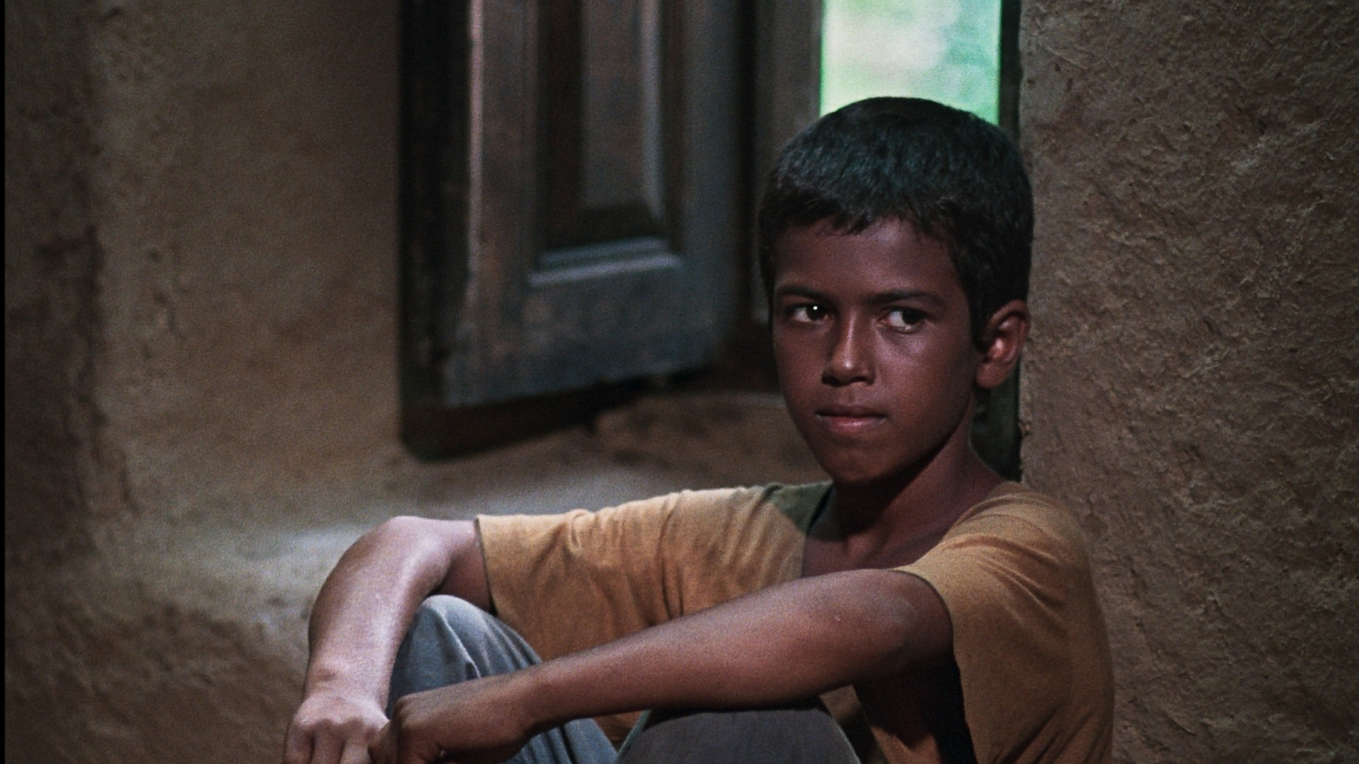 BASHU, THE LITTLE STRANGER, 1985, young boy in yellow t-shirt sitting on ground with arms resting on knees
