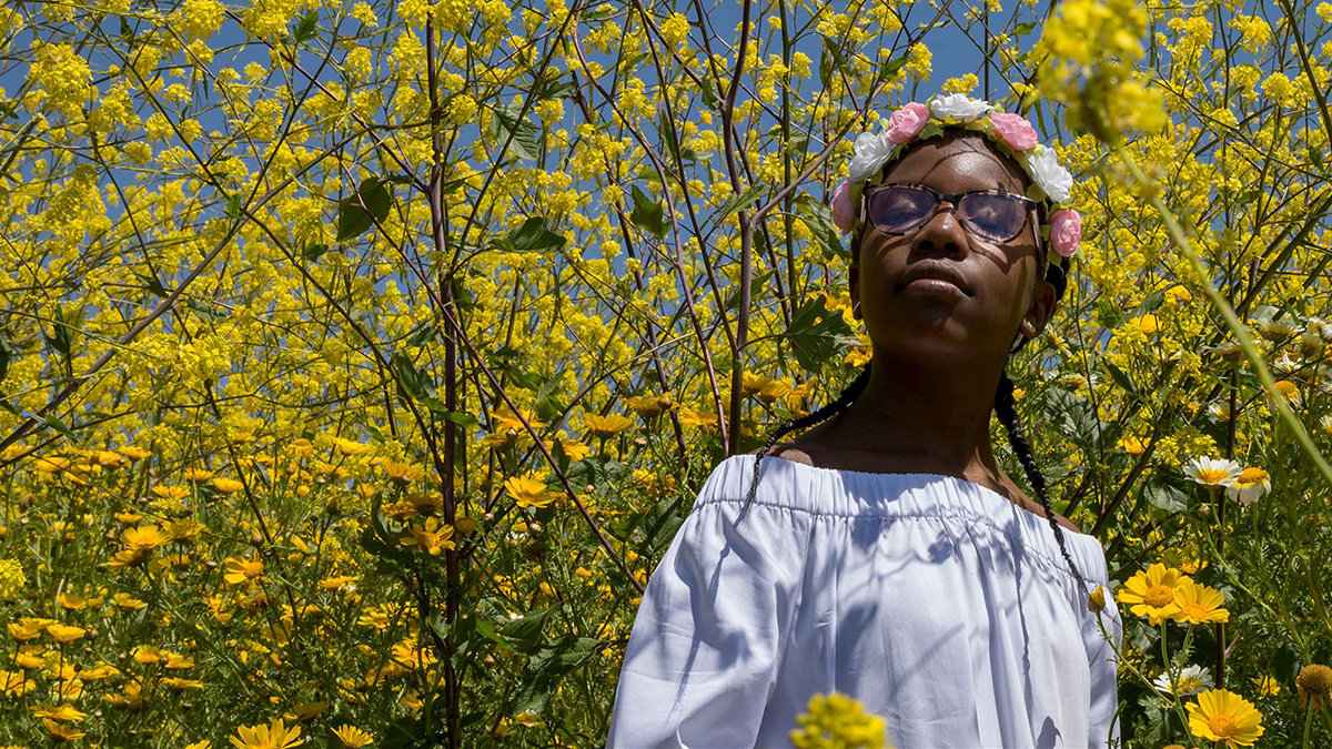 Person with flower crown in a field of flower, eyes closed