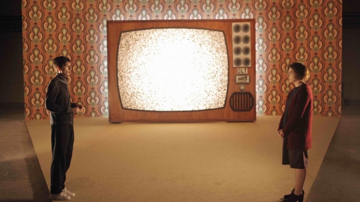 two people standing across from each other in front of large television