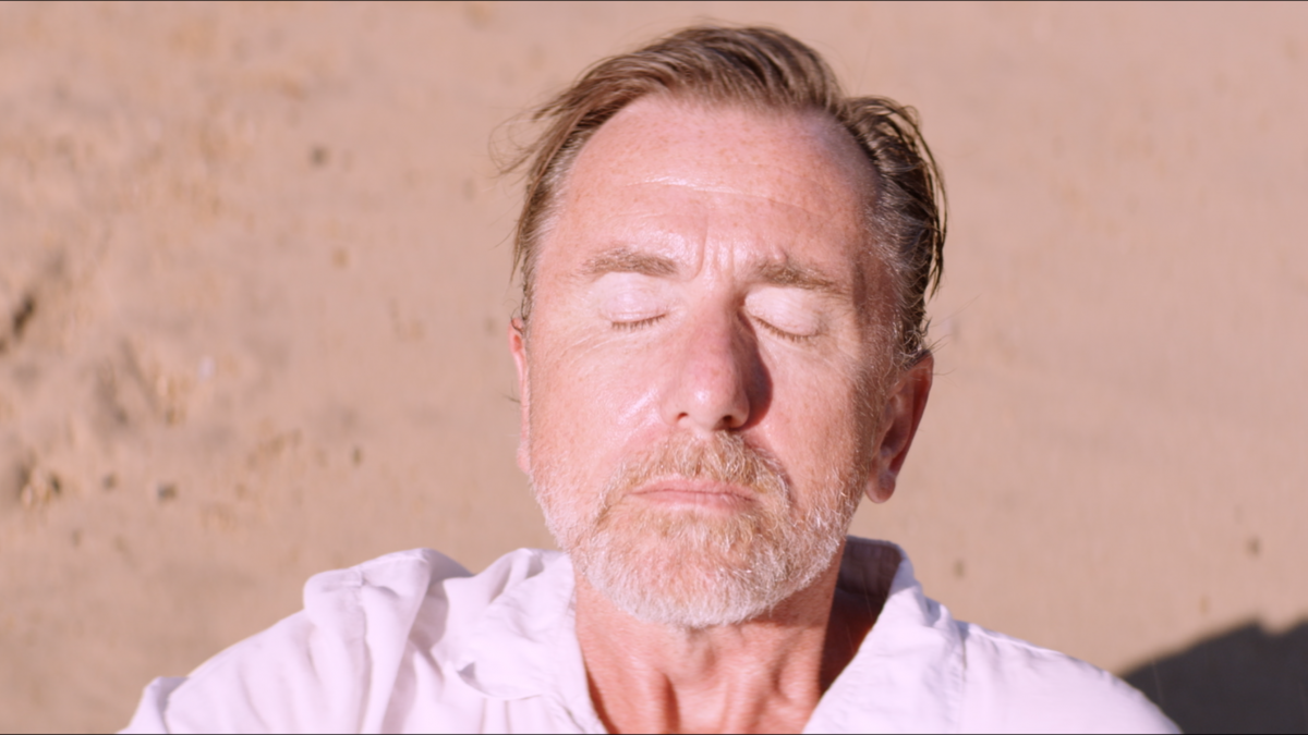 man staring up at sun with eyes closed on beach