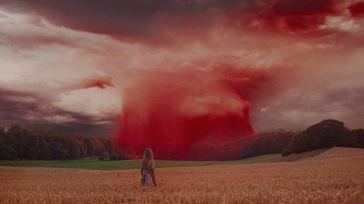 girl standing in field facing bright red sky
