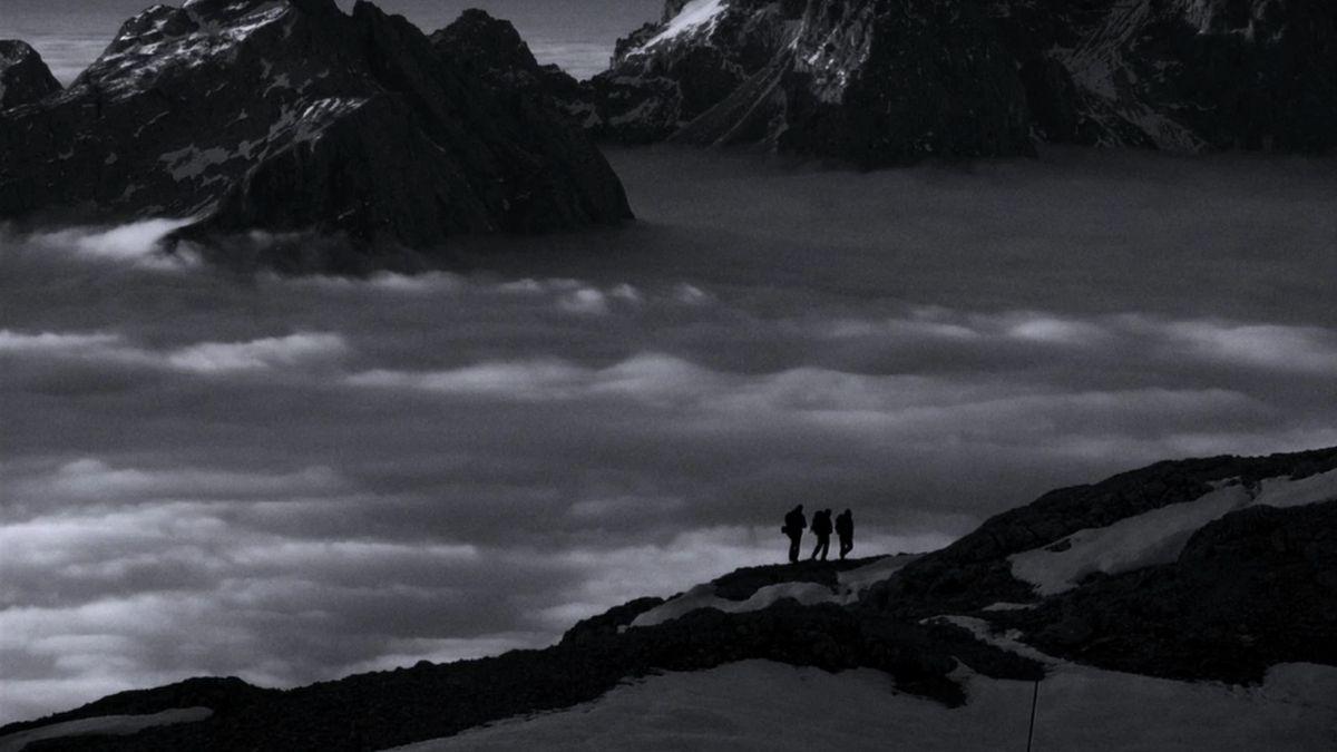 black and white ocean and mountains with three silhouettes in foreground