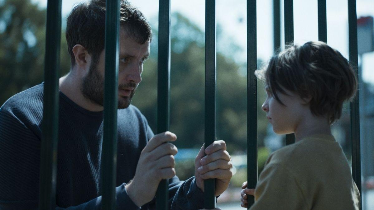 boy looking at man through bars in a fence with man holding bars on fence