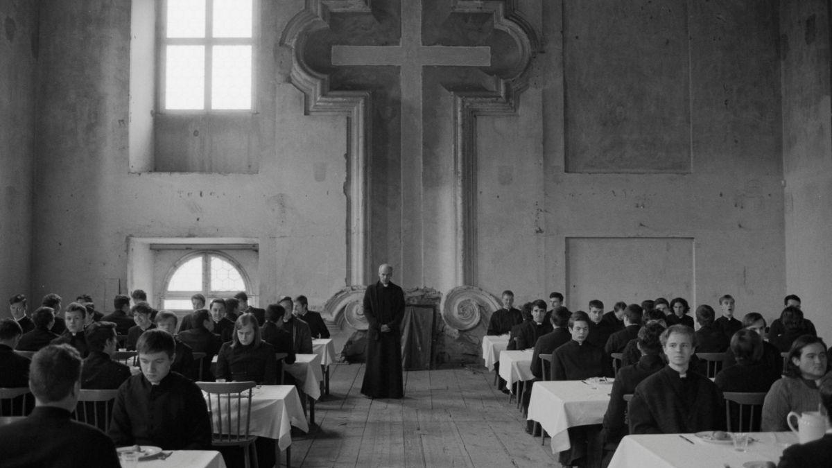 black and white photo of youth seated at tables with large cross in background