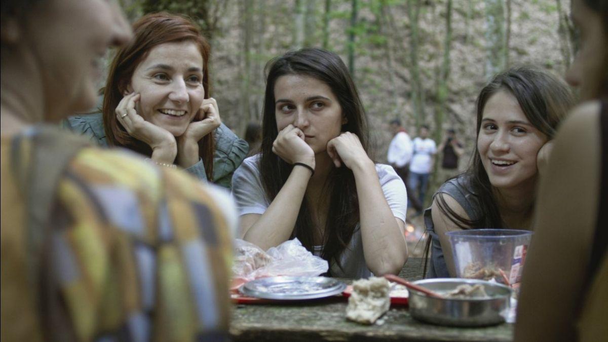 three women sitting at a picnic table in the forest conversing with hands on faces