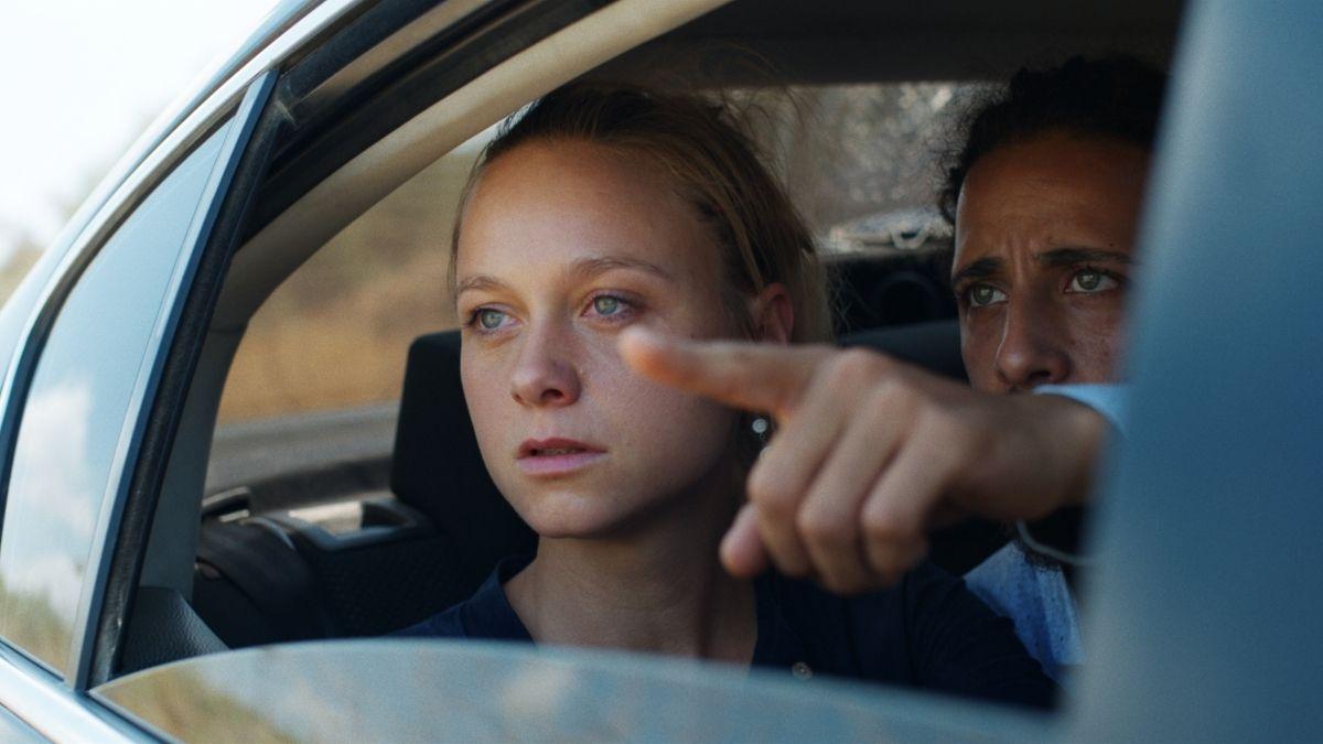 man and woman sitting in back of car with man pointing out of open car window
