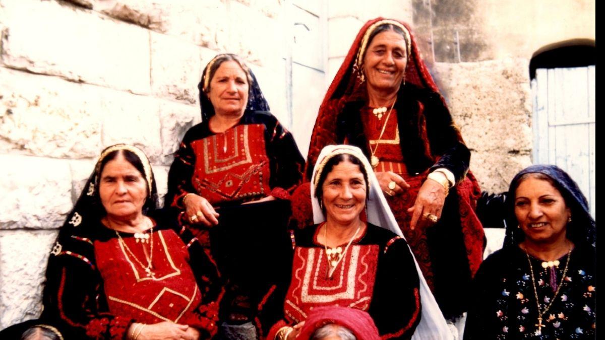 group of five women in traditional outfits sitting on steps