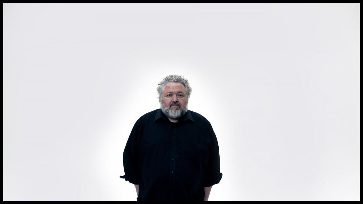 man with gray beard wearing all black standing in front of bright white background