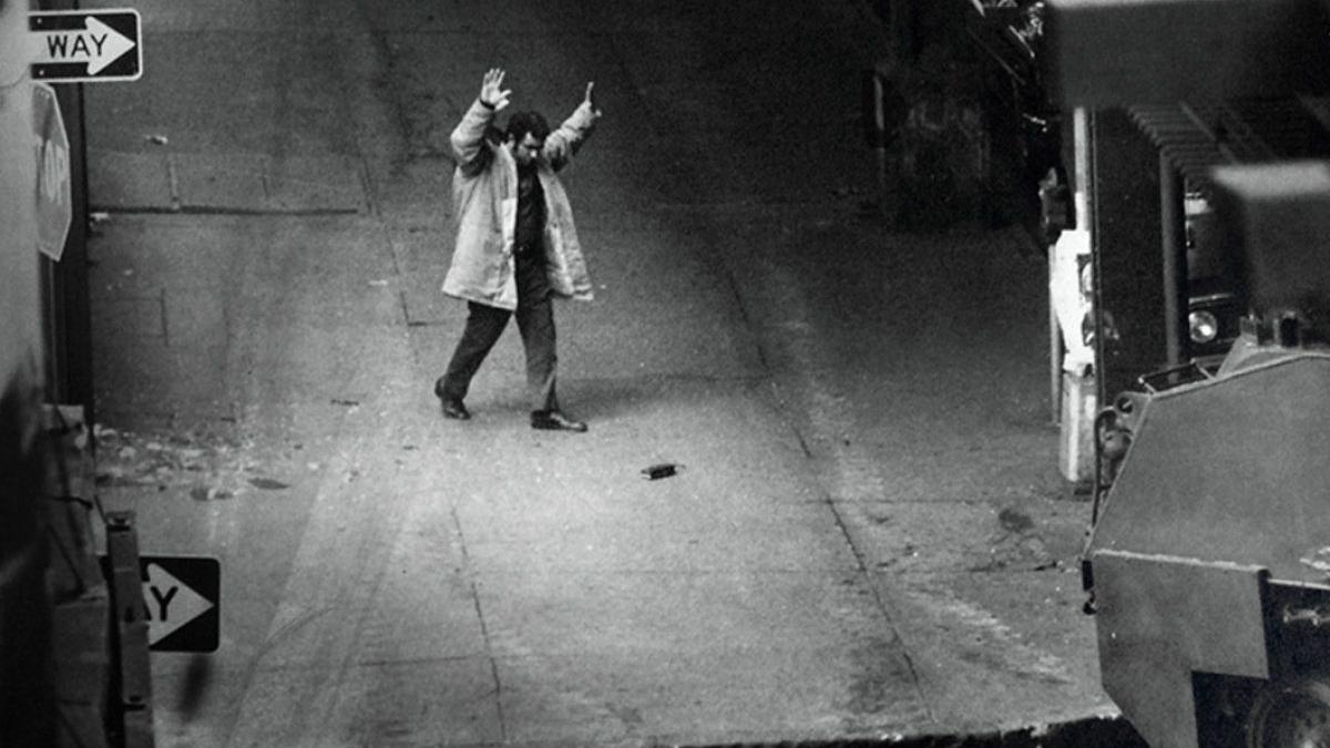 black and white image of man on street holding both hands above head