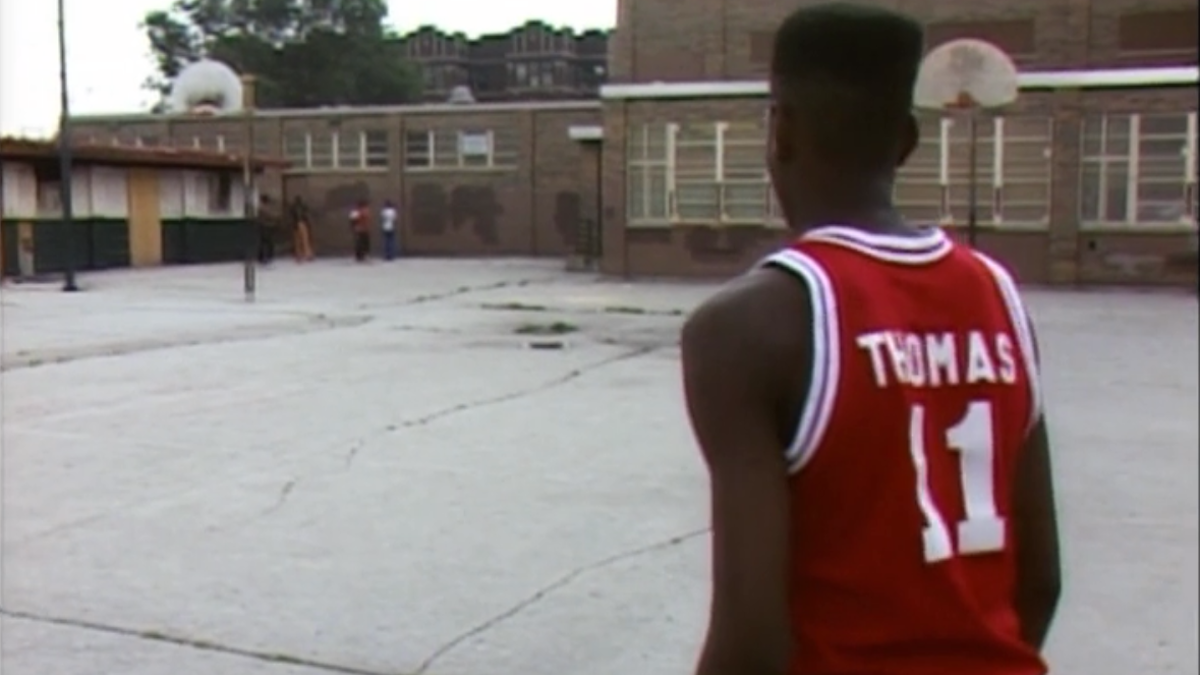 boy on outdoor basketball court wearing red basketball jersey