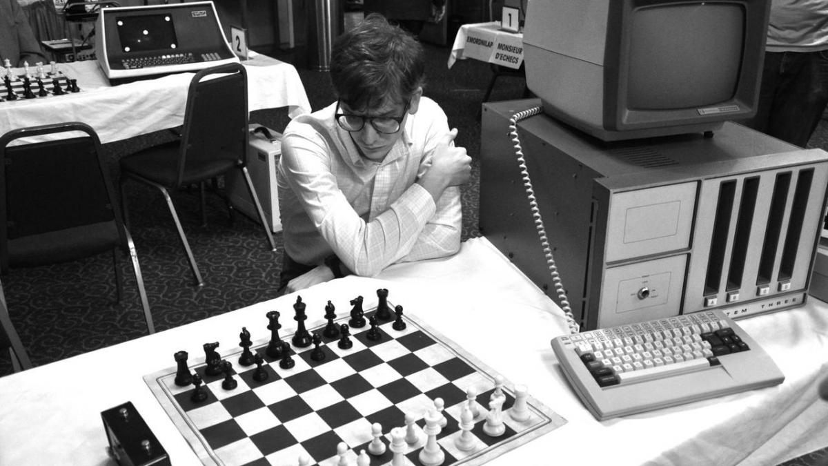 man looking at chess set next to computer and keyboard