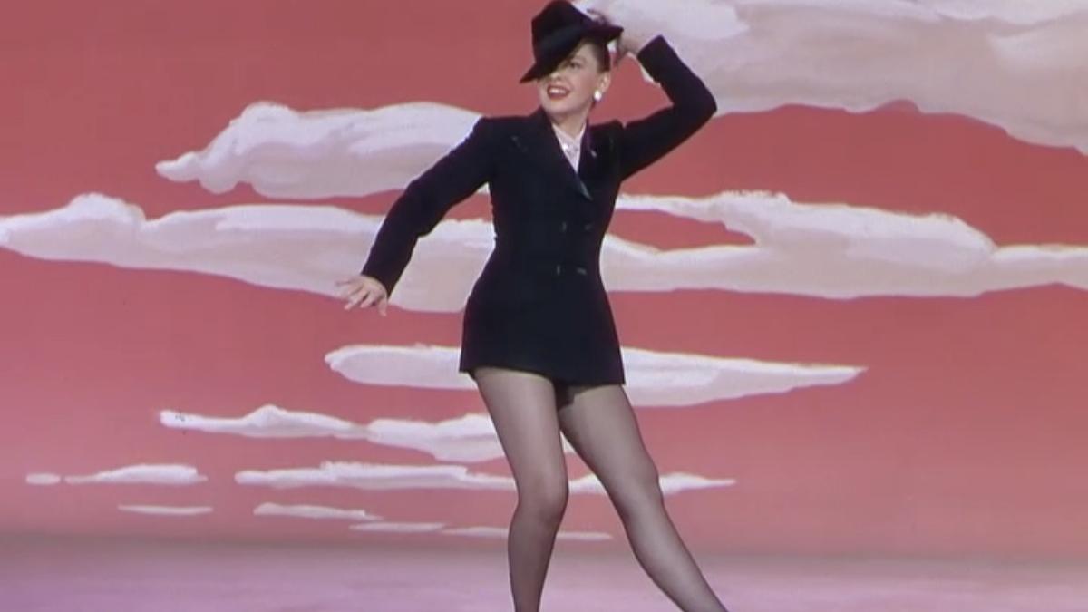 woman on stage in black costume dancing with hand on hat