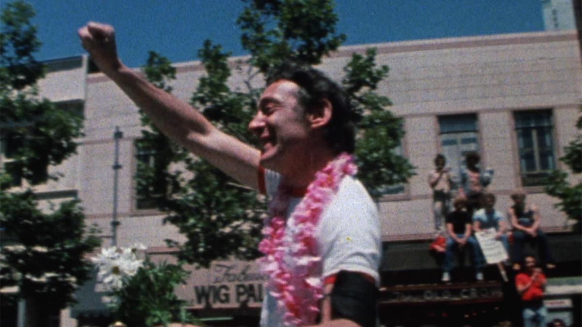 man in white shirt and lei holding hand up in fist in street parade