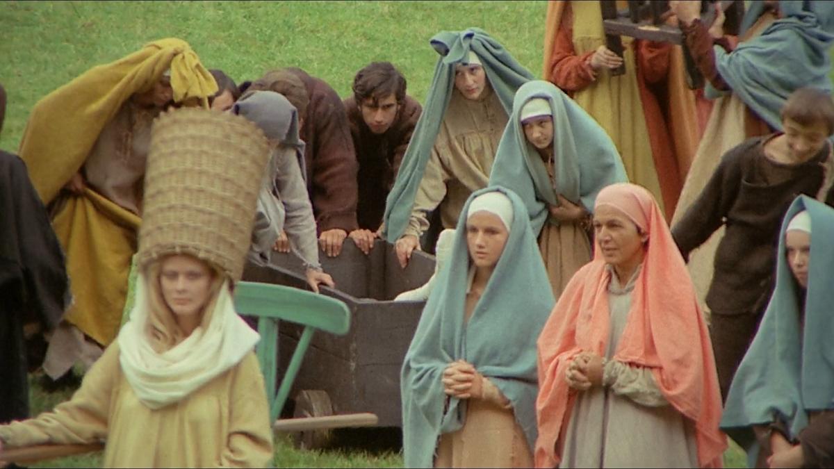 woman in field with large woven headdress and other women behind her with head scarves on