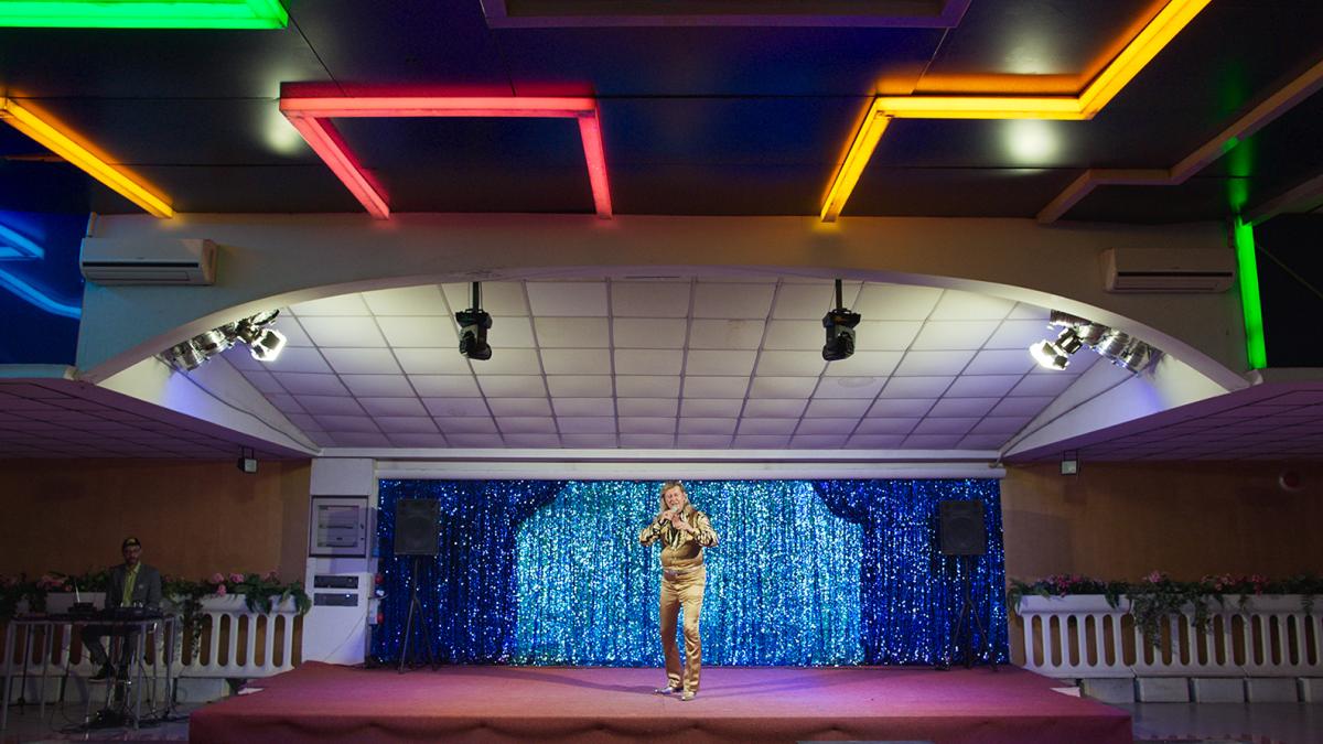 man standing brightly lit stage wearing colorful costume