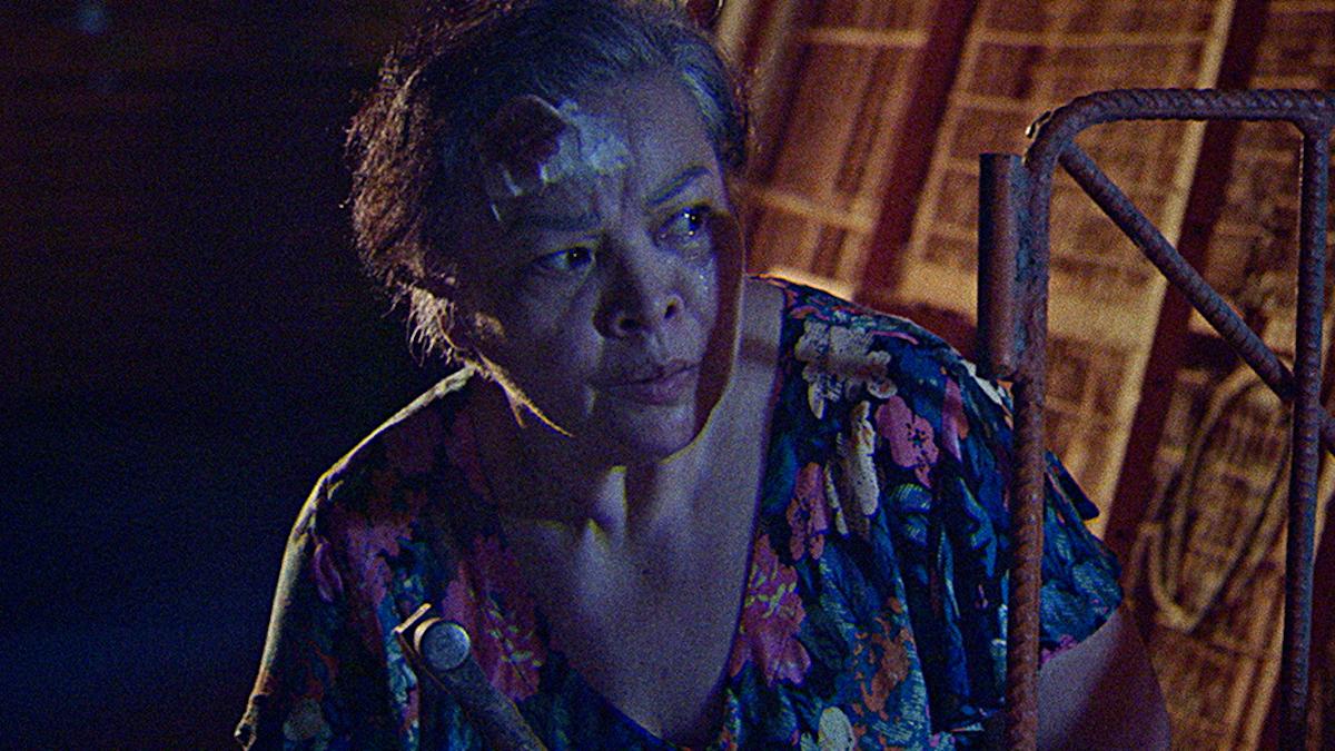 woman with bandage on forehead leaning over to look out window in dark