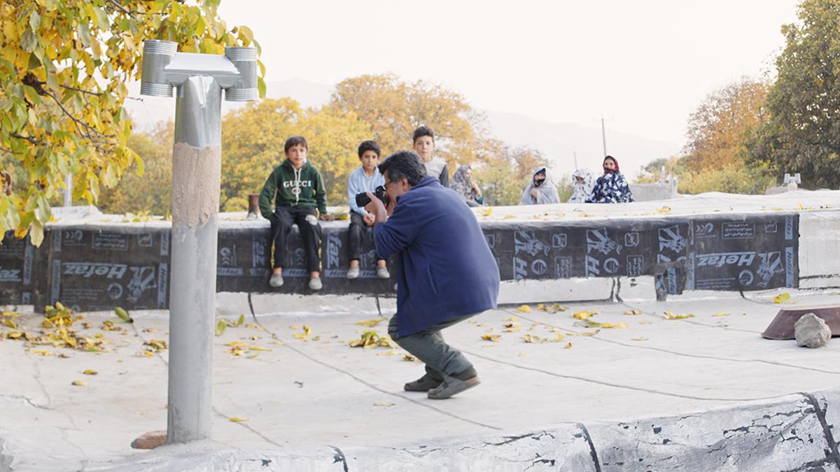 man in public park wearing dress clothes and squatting down aiming camera