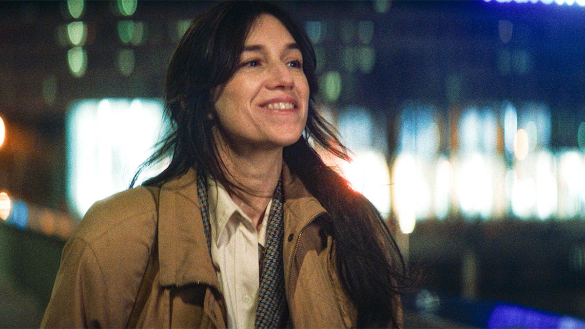 woman in brown coat smiling with city lights behind her