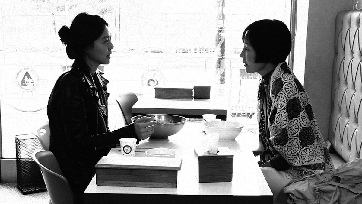 black and white image of two women sitting across from each other at booth in restaurant