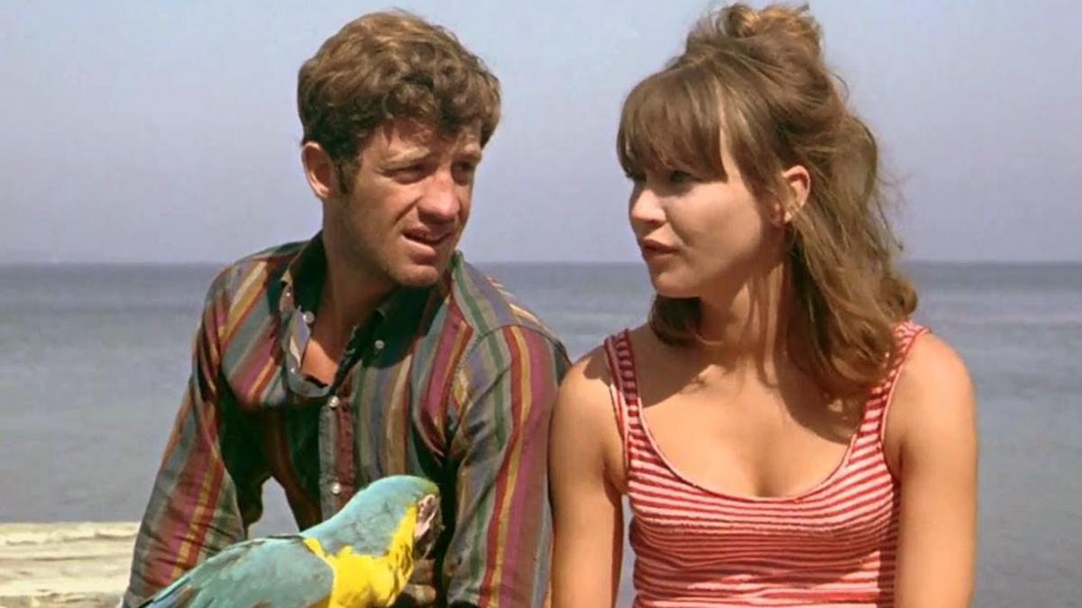 man and woman sitting by ocean with parrot