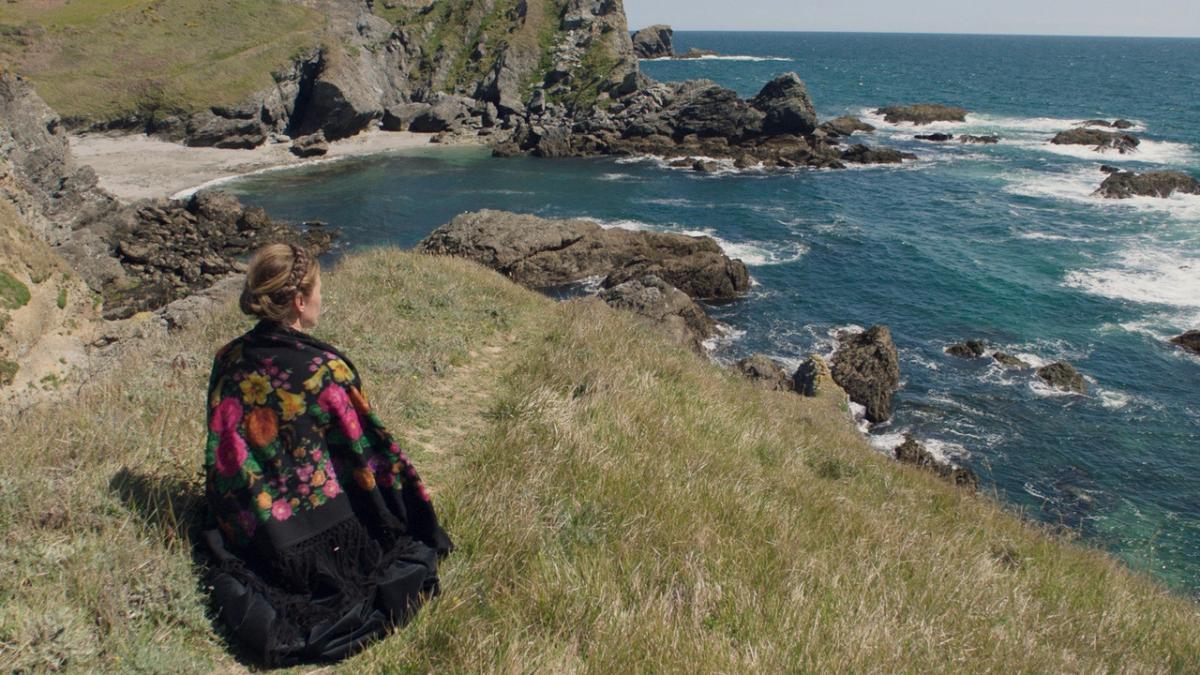 woman in black embroidered shawl sitting on top of hill looking out at sea