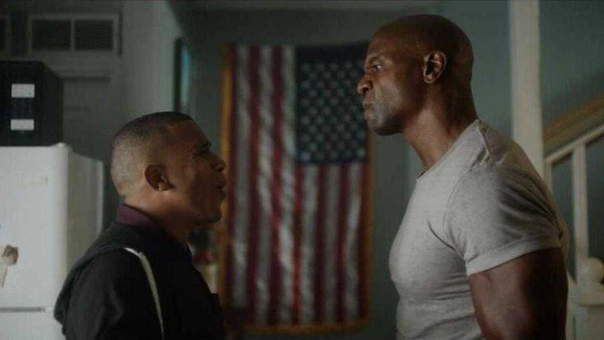 two men standing in kitchen staring at each other with american flag in the back