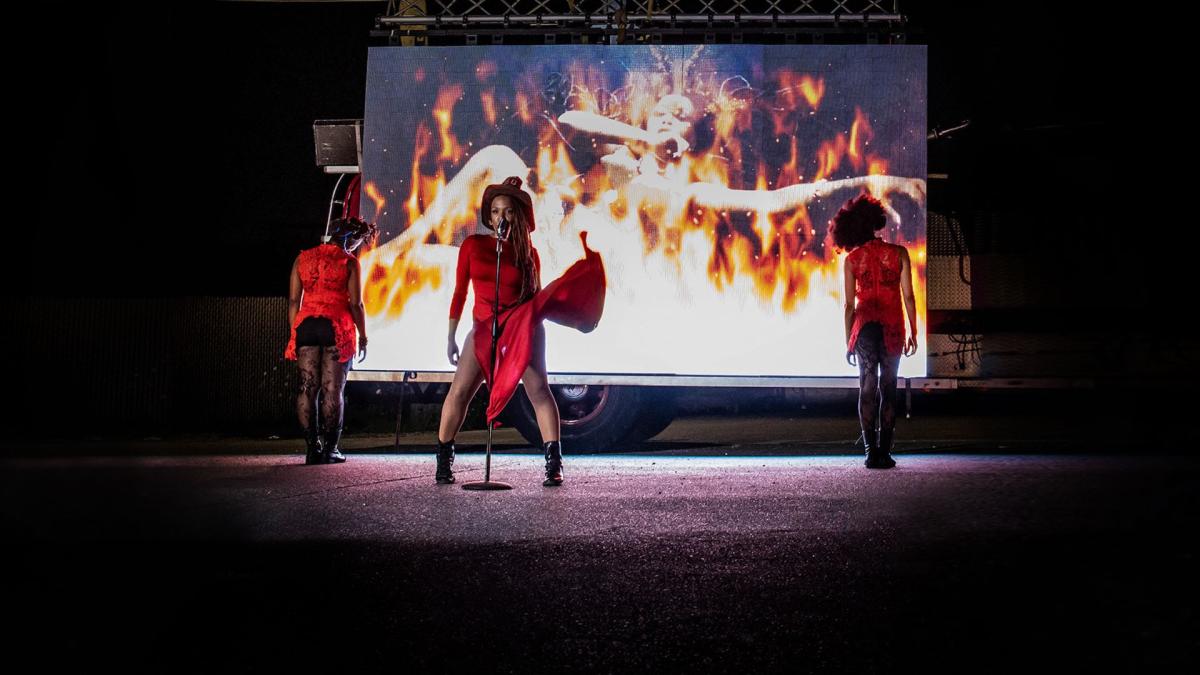 3 women in red dresses on stage with flame graphics behind them