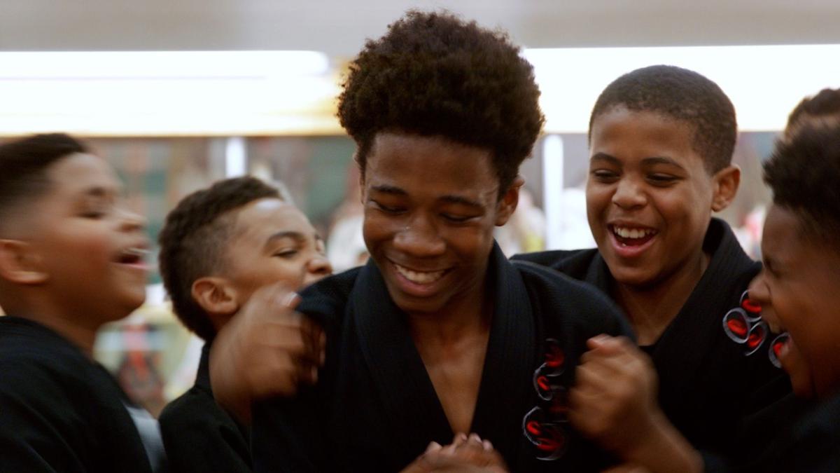 group of five boys smiling and cheering in martial arts uniforms
