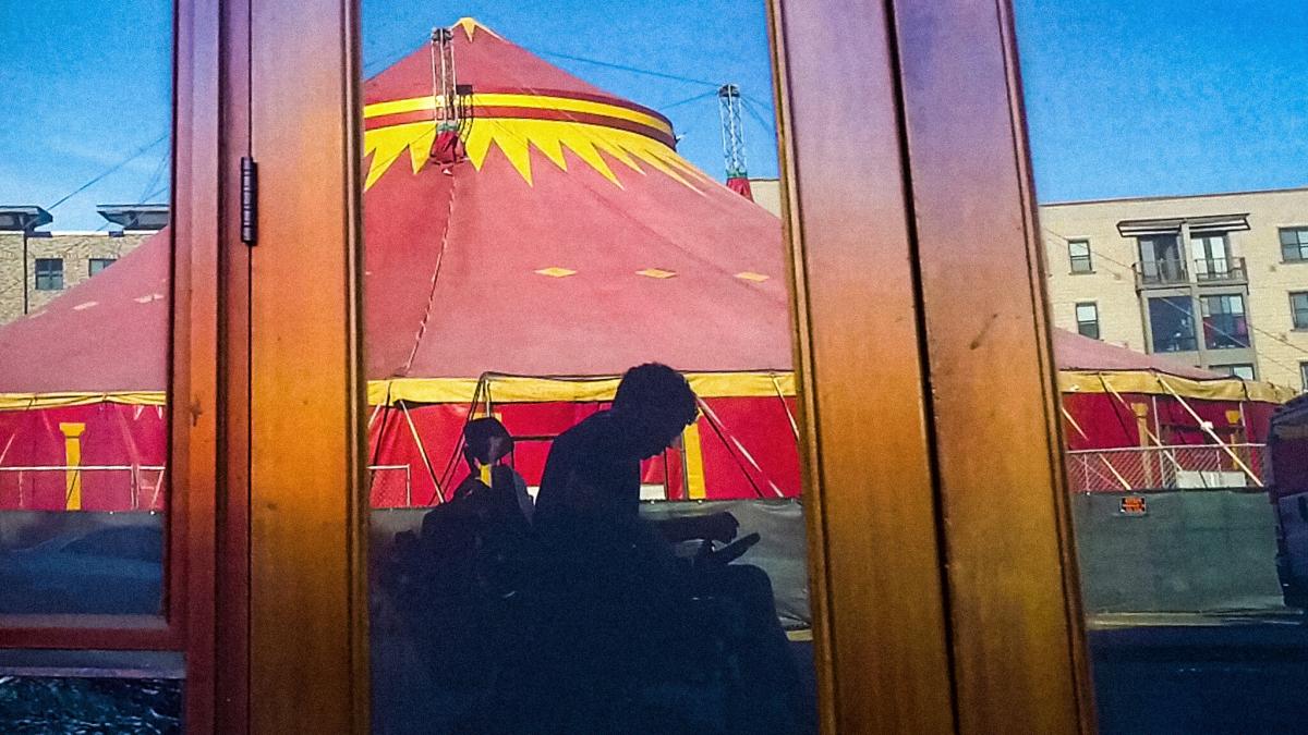 silhouette of person in wheel chair in the reflection with a carnival tent in background