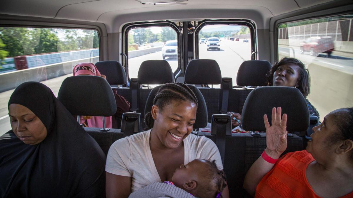 five Black women sitting in back of van with one in middle smiling and holding young child
