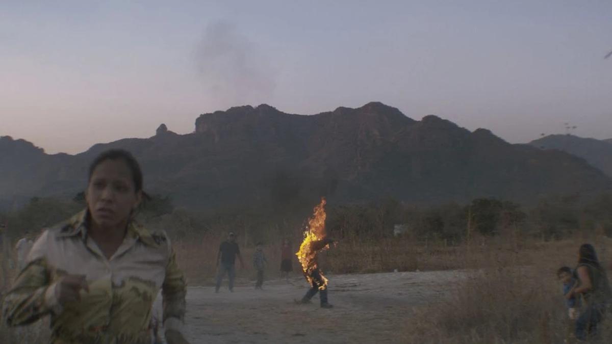 mountainous desert background, woman in foreground, man on fire in background