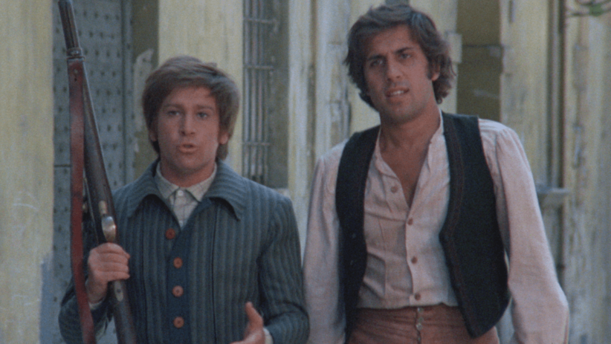 two men on street with one holding rifle