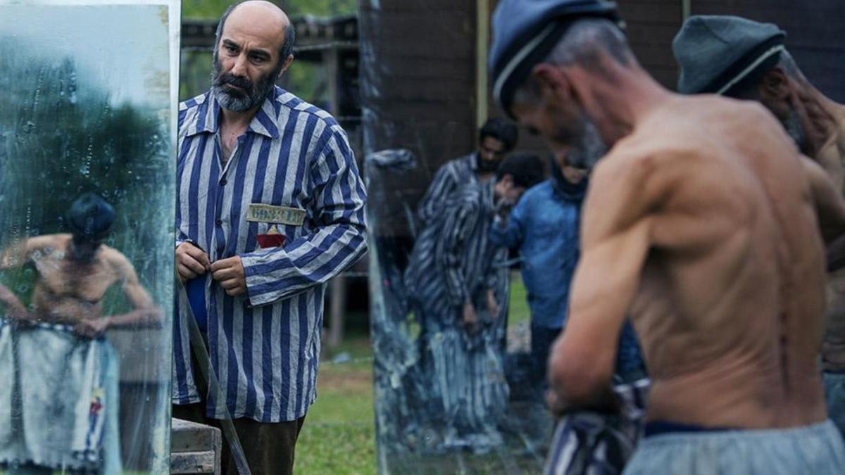 three men outside looking at glass with one shirtless and one wearing a striped uniform