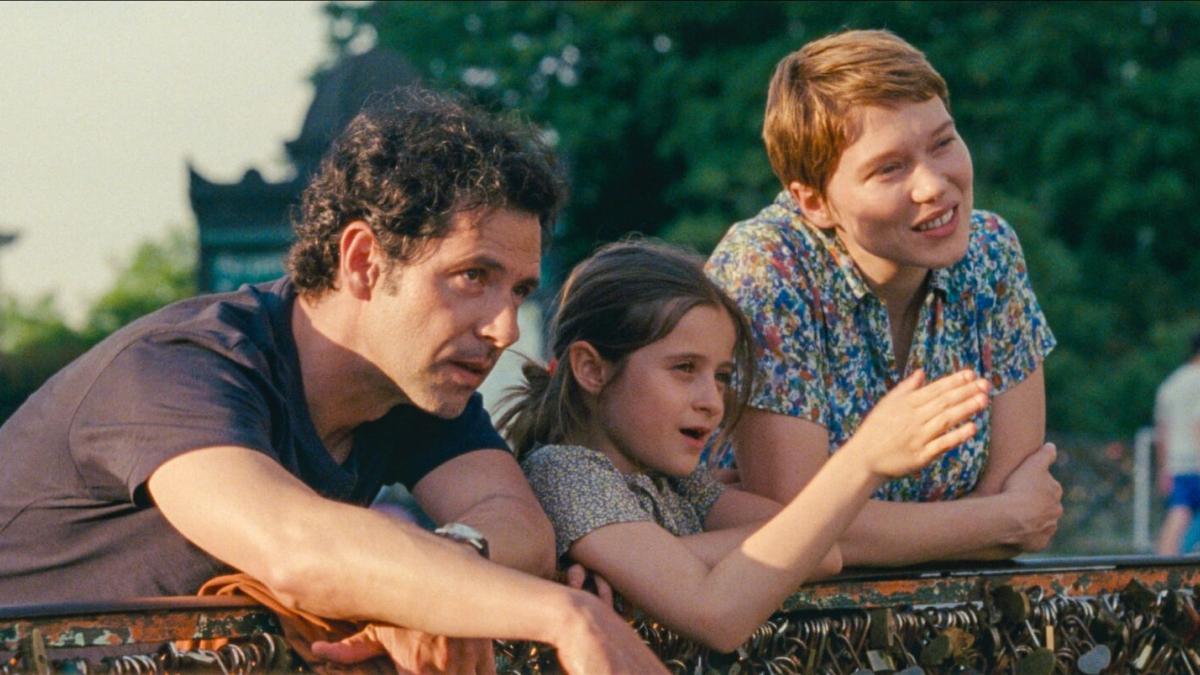 man, girl, and woman leaning over bridge pointing and looking into distance