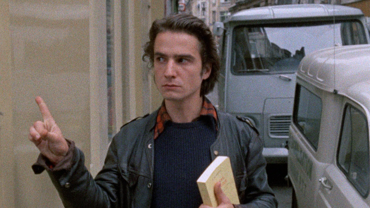 man walking down street with book under arm and finger pointed up